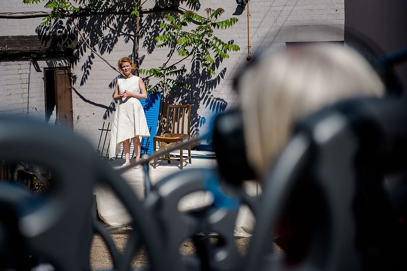 Photograph taken from behind seated audience on the bus, view of Jemima Foxtrot performing in an yard with garden furniture