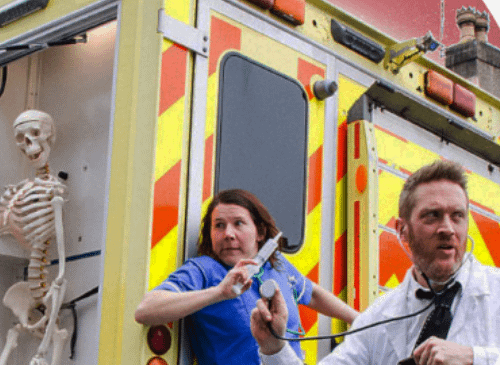 The image shows two people sat infront of an ambulance, pulling silly faces.