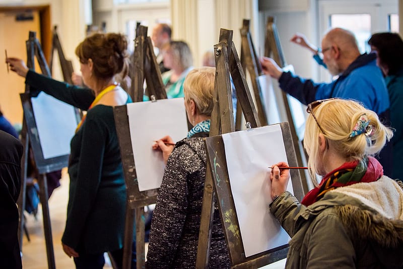 People holding pencils up to their canvases in a life drawing class