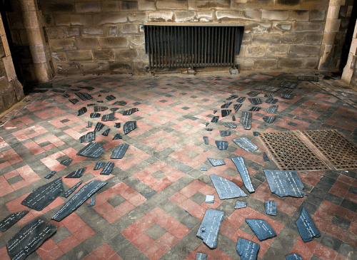 A row of slate sections sit on cobbled flooring. It looks like it's set in a church.