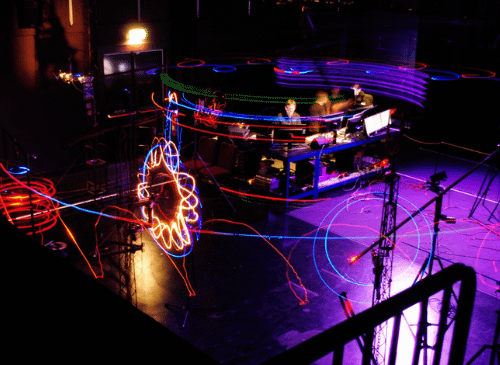 there is a light display in the middle of a dark room. The lights glow mostly purple, with a bright yellow light that looks like a flower. The image shows the movement of the lights and looks blurred in places.