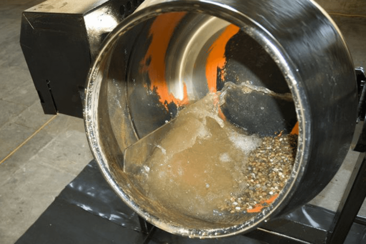 A metal cylinder has gravel and muddy water in the bottom of it. The inside of the metal drum has orange paint.