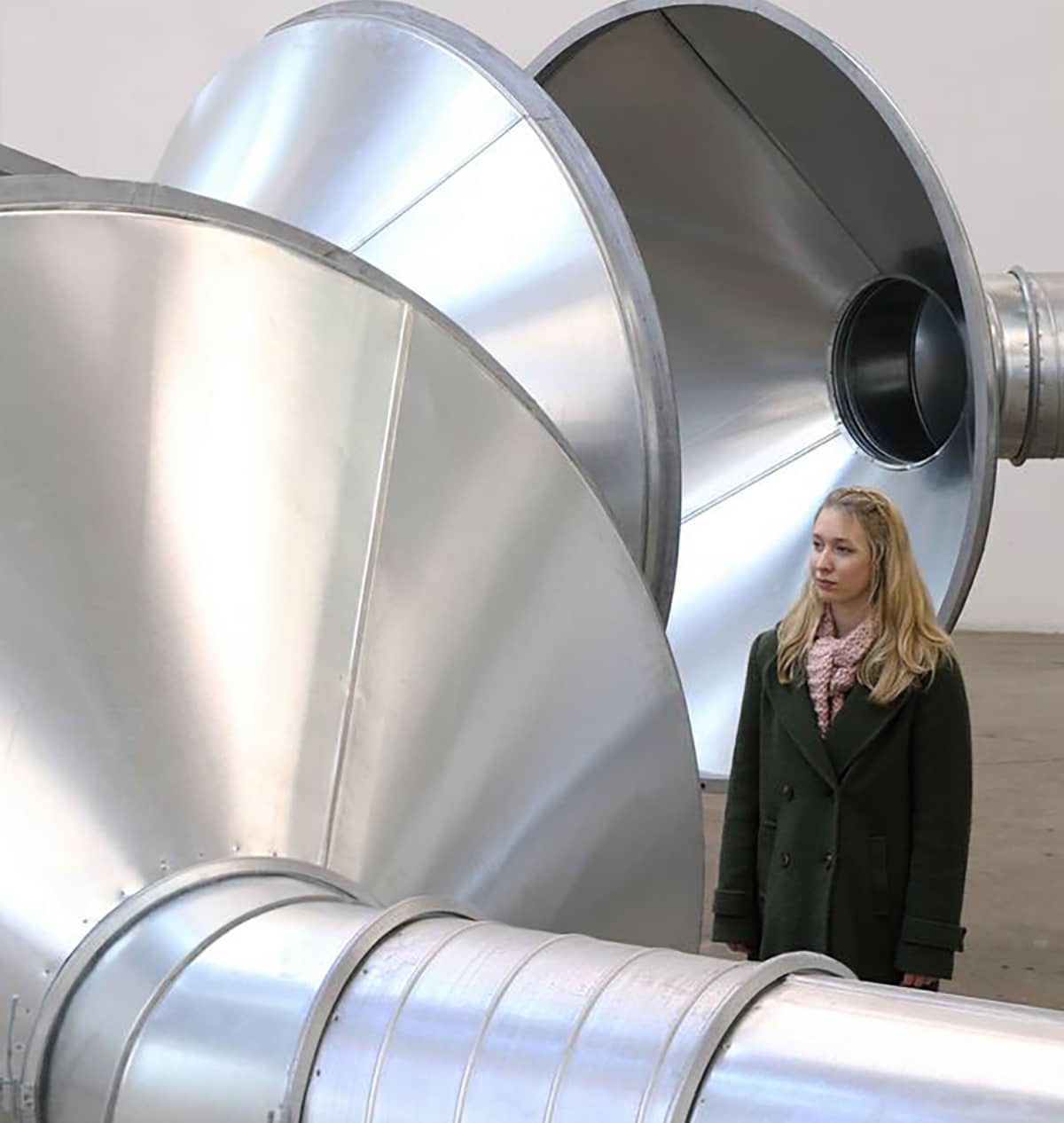Woman stands beside one of the speaking tubes, listening.