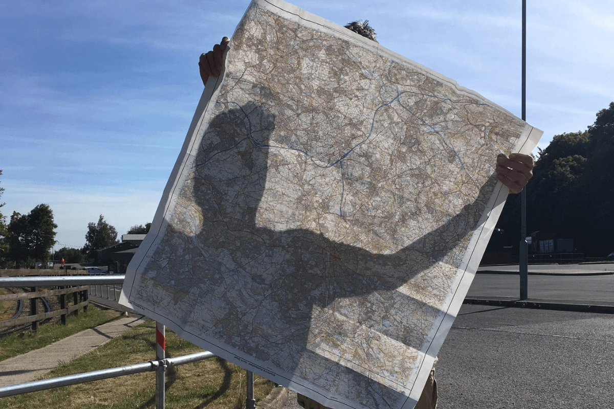 A figure holds a square map and casts a shadow over it while they holds it.