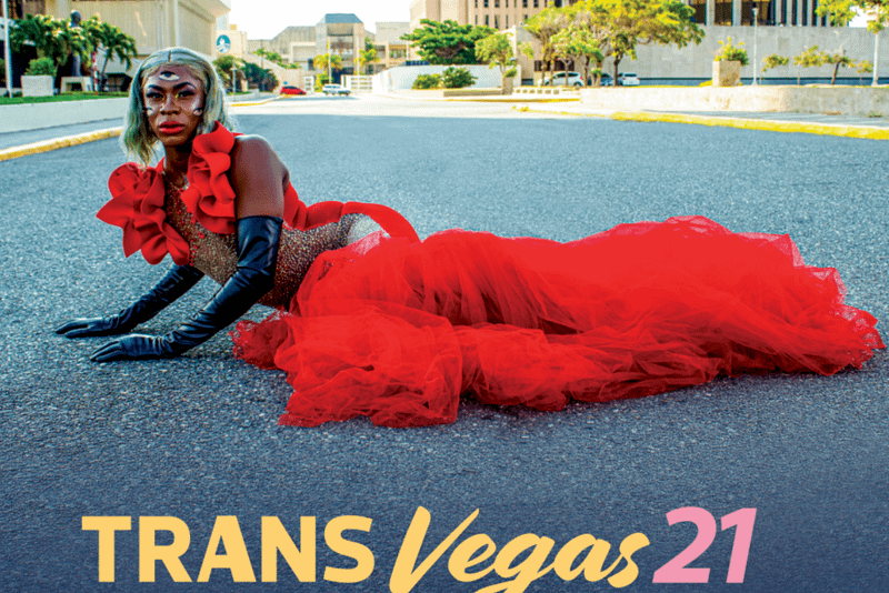 A person lies sideways on the floor. They have a red dress on, and black gloves. Underneath the image are the words Trans Vegas 21
