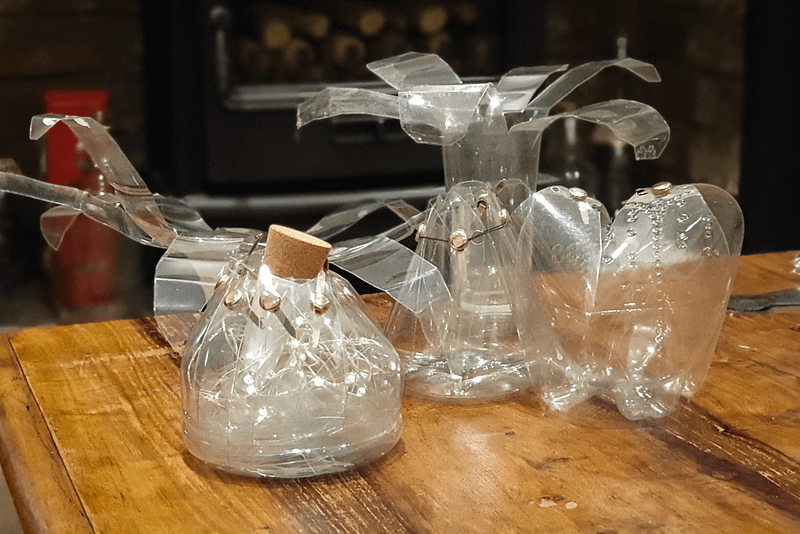 A series of bottles sit on a wooden table, they are shaped into different forms.