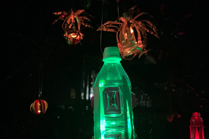 A green bottle is lit up with a background of dark trees and orange lights.