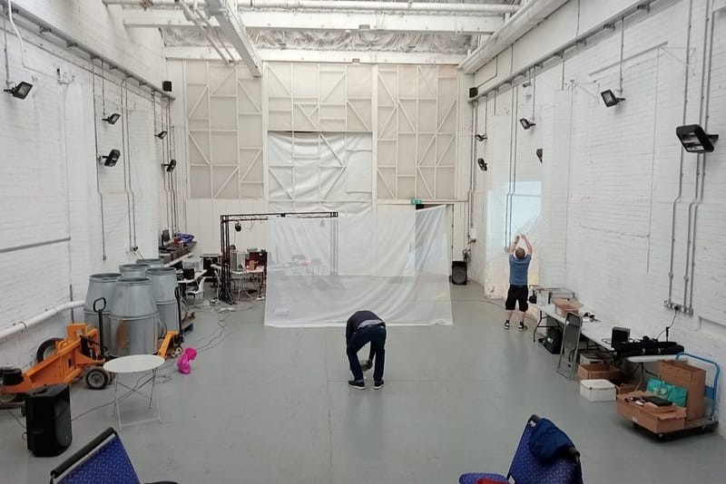 Long view of a large white industrial look studio with men setting up a screen