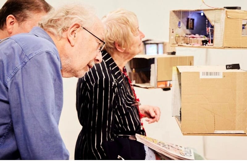 Two elderly people looking a cardboard miniture house in an exhibition