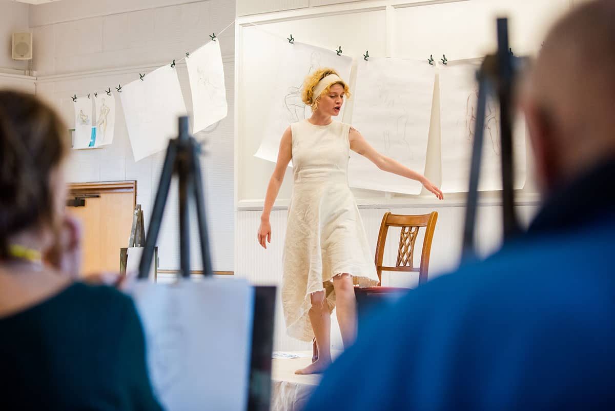 Performer Jemima Foxtrot at front of life drawing class in white dress, the costume from the Rear View performance