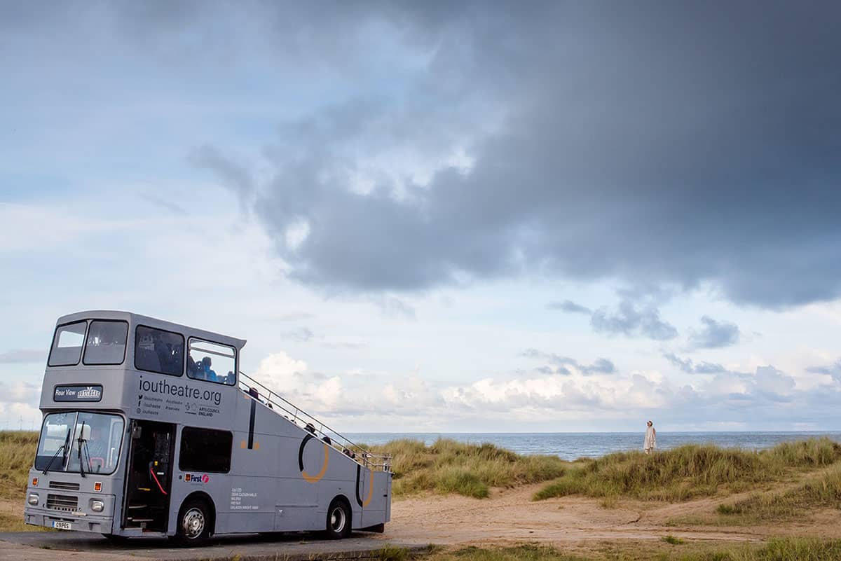 Rear View Bus parked at sea front with performer Jemima Foxtrot on far horizon