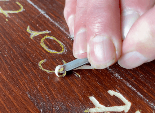 A close up image of someone using a chizel to carve letters on a piece of wood.