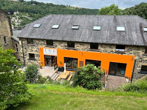 http://There%20is%20a%20large%20stone%20building,%20with%20a%20bright%20orange%20panel%20on%20the%20front.%20There%20are%20trees%20in%20the%20background,%20and%20a%20blue%20sky%20above%20the%20trees.