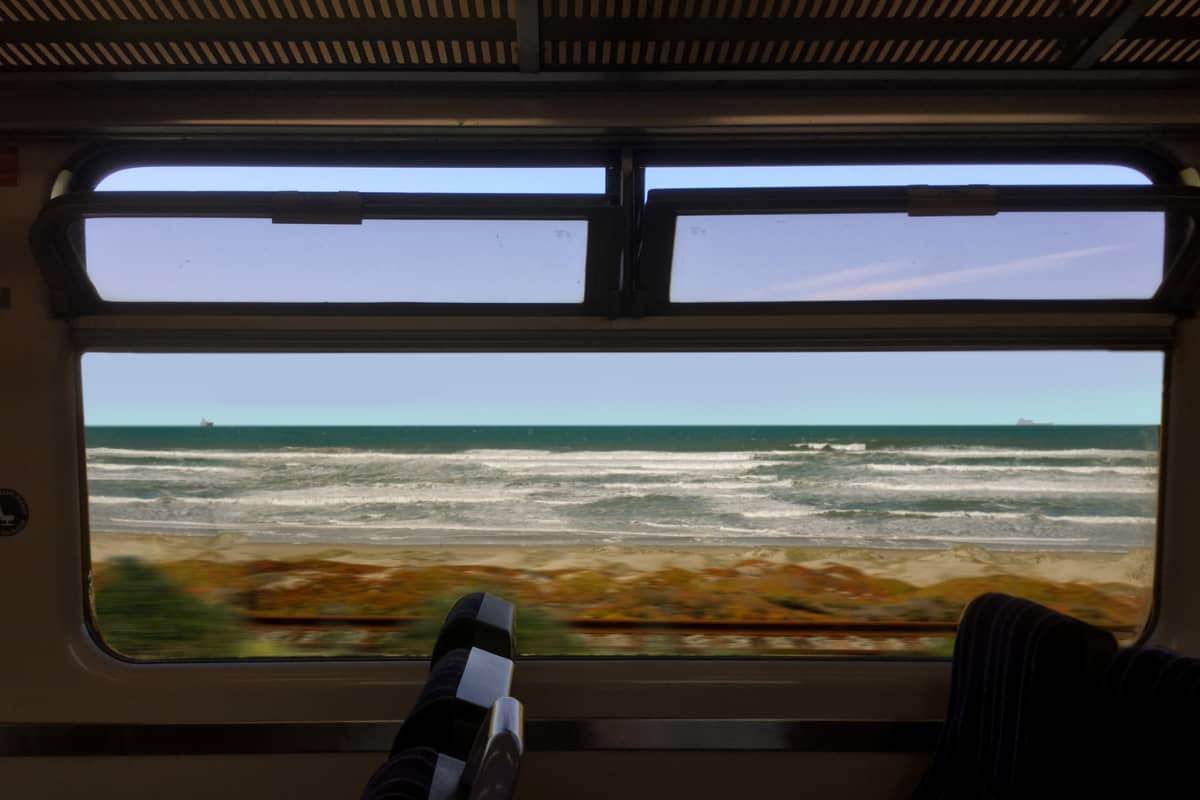 Out of a train window there are waves showing the sea, you can see the tops of chairs in front of the window.