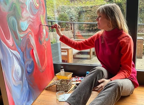 woman in red sweater paints a multi coloured oil painting